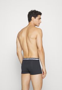 Gray boxer shorts with a white branded waistband, shown on a model from the back. The material appears smooth and form-fitting.