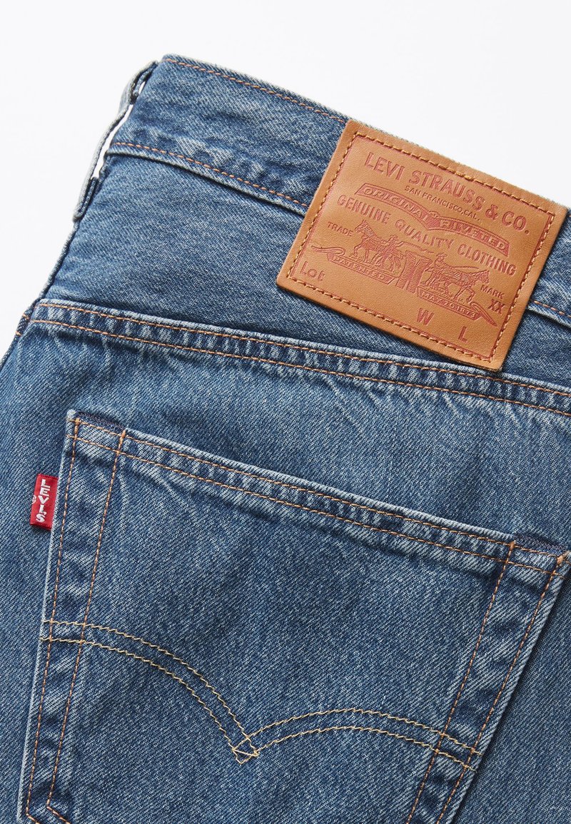 Hellblaue Denim-Jeans mit texturiertem Finish. Verfügt über ein braunes Leder-Patch mit Markenlogo am hinteren Bund und ein rotes Logoband.