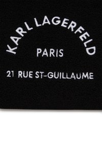 Zwarte stof met witte geborduurde tekst: "KARL LAGERFELD," "PARIJS," en "21 RUE ST-GUILLAUME." Zachte textuur met een strak ontwerp.