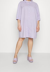 Lavendelfarbenes Knopfkleid mit einem Kragen und dreiviertellangen Puffärmeln, kombiniert mit passenden offenen Plateauschuhen. Glatte Textur.