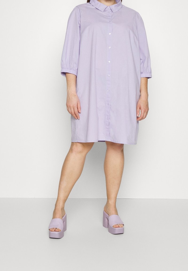 Lavendelfarbenes Knopfkleid mit einem Kragen und dreiviertellangen Puffärmeln, kombiniert mit passenden offenen Plateauschuhen. Glatte Textur.