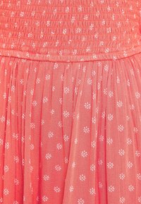 Korálové šaty s nařaseným tělem a skládáním sukně, zdobené bílými květinovými vzory na lehkém materiálu.