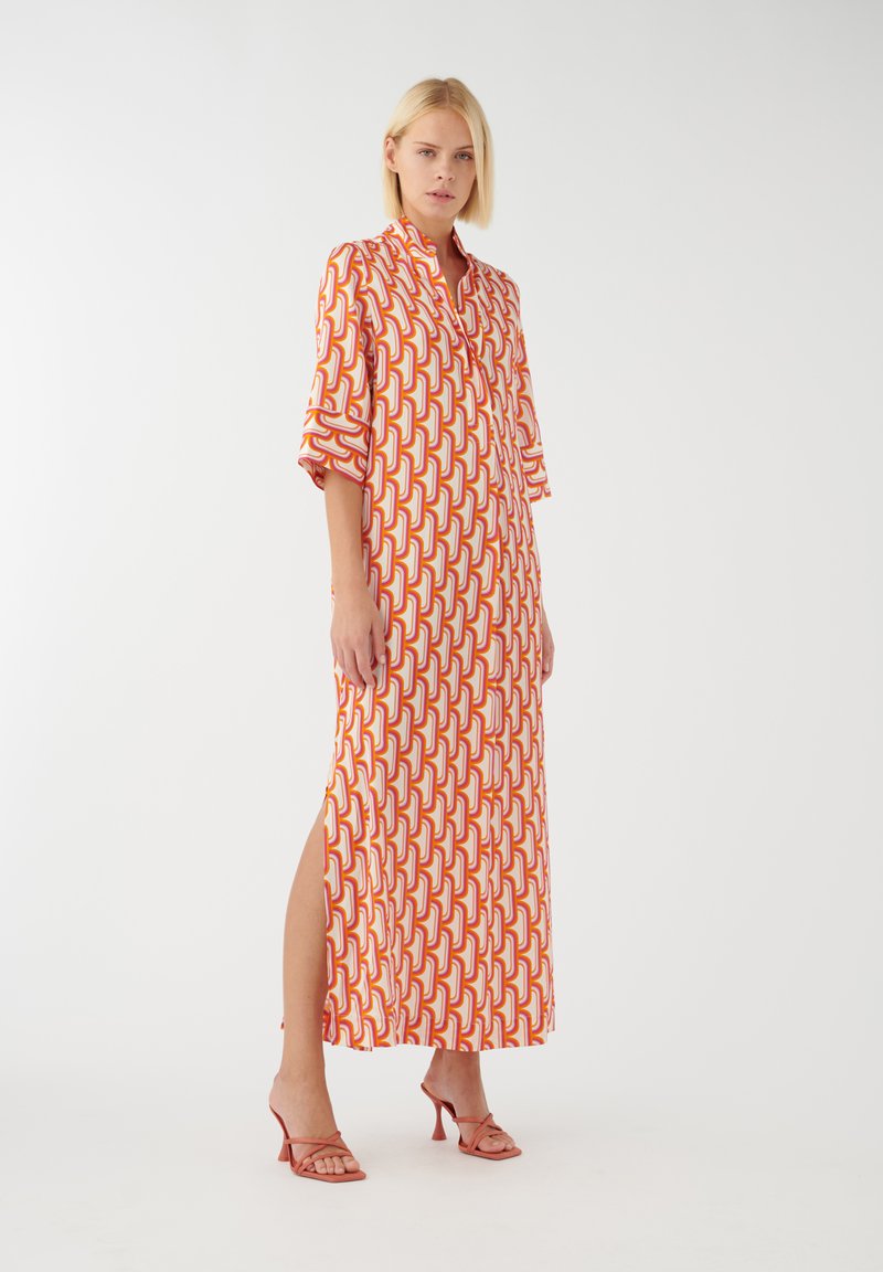 Maxikleid in Orange und Creme mit einem geometrischen Muster, verfügt über einen Kragen und einen seitlichen Schlitz, gefertigt aus leichtem Stoff. Hochhackige Sandalen sind enthalten.