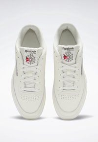 Ett par vita Reebok Classic låga sneakers med snörning, perforeringar på tån och logotyp på tungan och sidan.