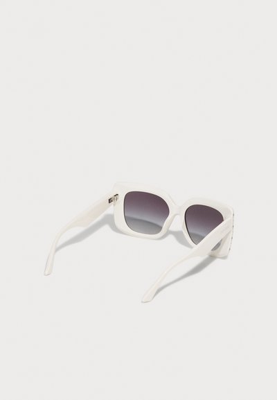 Lunettes de soleil rectangulaires blanches avec des montures épaisses et des verres dégradés foncés reposant sur une surface claire.