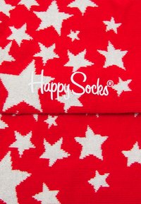 Røde sokker med hvide stjernemønstre, der har en skinnende tekstur. Mærkenavnet "Happy Socks" vises tydeligt i hvid.