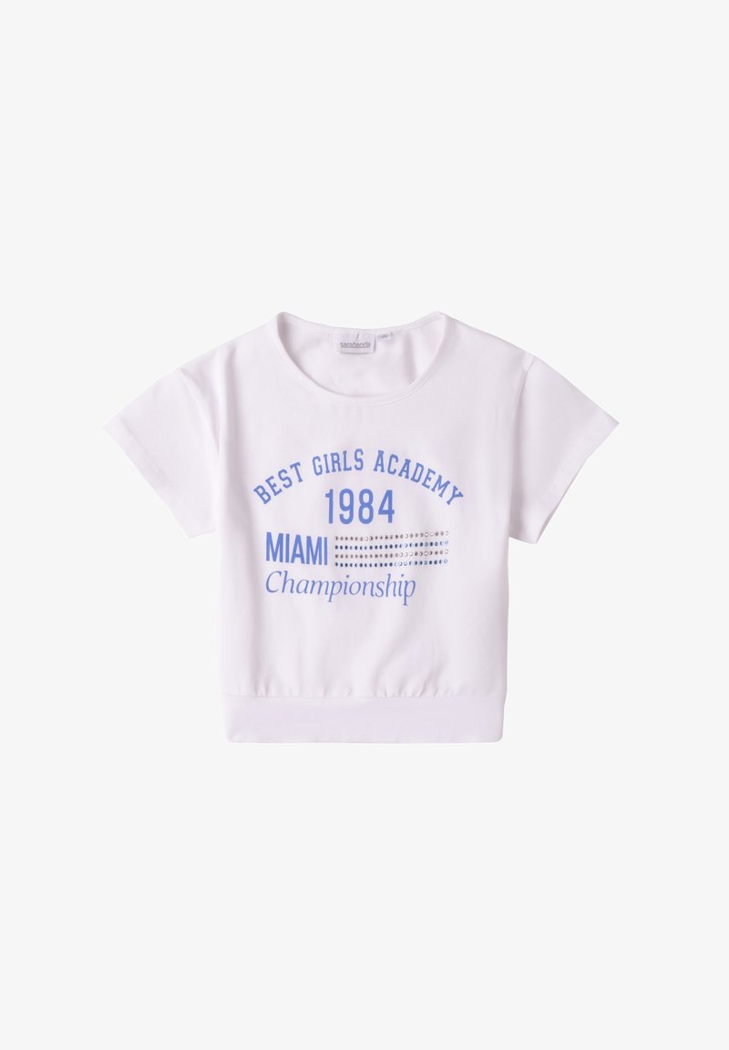 Top corto de manga corta blanco, hecho de algodón suave, que presenta texto impreso en azul: "ACADEMIA DE LAS MEJORES CHICAS 1984 CAMPEONATO DE MIAMI" con acentos decorativos.