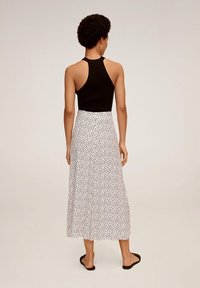 Sort ribbet tanktop parret med en hvid, knælang nederdel med et spredt sort prikmønster. Enkle flade sandaler fuldender outfittet.