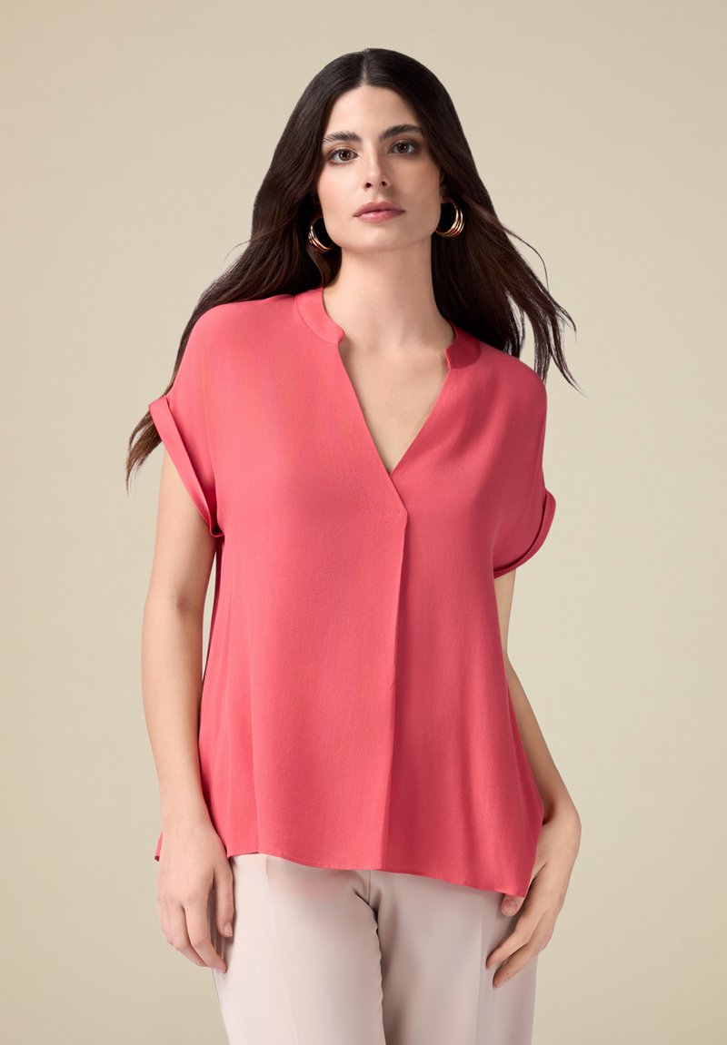 Koraalblouse met een V-hals en korte opgerolde mouwen; lichtgewicht stof met een relaxte pasvorm en subtiele draping; gladde textuur.