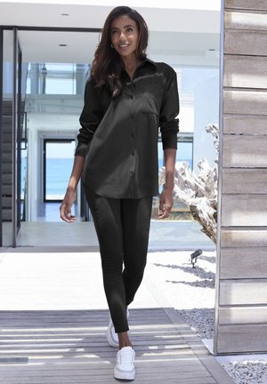 Schwarzes Hemd mit hochgekrempelten Ärmeln, kombiniert mit schwarzen Leggings und weißen Sneakers. Glatter Stoff, lässiges Design und taillierte Silhouette.