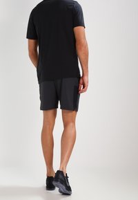 Camiseta atlética negra y pantalones cortos oscuros con bolsillos, combinados con zapatillas negras. El tejido parece suave y ligero.