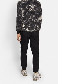 Pantaloni cargo neri con gambe affusolate abbinati a un felpa in pile bianco e nero con effetto tie-dye e sneakers di colore chiaro.