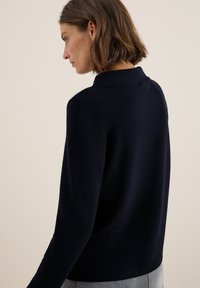 Marineblaues Langarmoberteil mit Kragen und glatter Textur, das eine enganliegende Silhouette und ein minimalistisches Design aufweist.