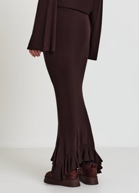 Dunkelbrauner, gerippter langer Rock mit ausgestelltem Saum und Rüschen am unteren Rand, kombiniert mit braunen, strukturierten Stiefeln.