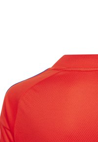 Polo shirt de sport rouge avec un tissu texturé, un col classique et des accents bleus le long des coutures d'épaule.