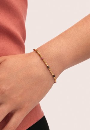 Goldfarbener Perlenarmreifen mit kleinen schwarzen und rosa Perlen, die an einem Handgelenk präsentiert werden. Glatte Textur, zartes Design mit wechselnden Farben.