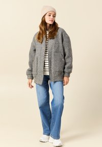 Veste en laine grise texturée avec deux poches avant, poignets côtelés et col. Associée  à un jean bleu clair et des baskets blanches.