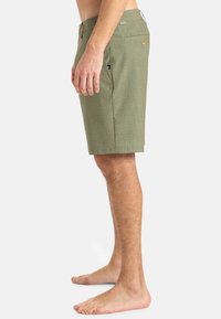 Zelené šortky s textúrovaným vzorom, dĺžka po kolená. Obsahujú bočné vrecká, zapínanie na gombík a malý detail loga na páse.