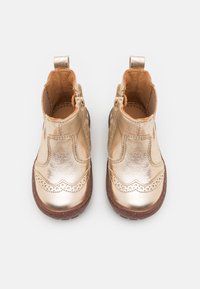Bottines dorées métalliques avec une texture lisse, des détails brogue et des semelles brunes contrastantes. Équipées de fermetures éclair et de boucles au talon pour un enfilage facile.