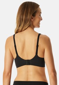 Reggiseno nero con spalline regolabili, design con schiena arrotondata, chiusura con gancio e asola, e texture in tessuto liscia. Nessun abbellimento aggiuntivo presente.