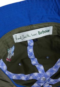Εσωτερικό μπλε και ελιάς κάπας με μπλε καρό περιθώριο, μεταλλικά ανοίγματα αερισμού, κεντημένο λογότυπο και ετικέτα με την επιγραφή "Paul Smith αγαπάει Barbour."