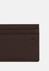 Brown leather cardholder featuring multiple card slots, neat stitching, and a debossed logo on the front. Smooth texture with a sleek design.