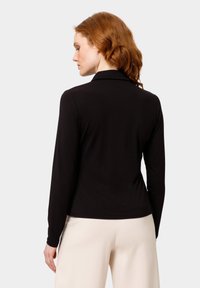 Černá košile s dlouhým rukávem a límečkem, hladká textura, přiléhavý střih a subtilní detaily šití, v kombinaci s světlými kalhotami.