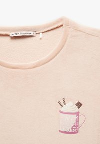 Pull en polaire rose clair avec un col rond et un graphique d'une tasse avec de la crème fouettée et des accents chocolatés. Étiquette de taille S visible.