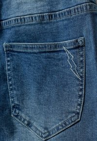 Plava traper tkanina koja sadrži stražnji džep s karakterističnim šavom u obliku munje. Tekstura je blago izblijedjela i glatka.