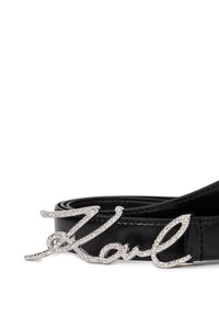 Curea din piele neagră, dotată cu o cataramă lucioasă de culoare argintie, pe care se află un design cursiv "Karl", ornate cu strasuri.