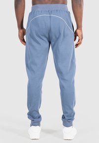 Modré tepláky z měkké látky s úzkým střihem, bílé akcentní švy a žebrované manžety, v kombinaci s bílými teniskami.