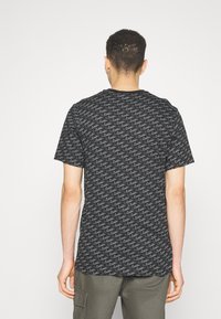 Černé tričko s krátkým rukávem, které má opakující se vzor vln s šedými akcenty. Vyrobeno z měkké tkaniny s designem kulatého výstřihu.