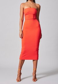 Robe midi orange sans bretelles avec une silhouette ajustée, texture côtelée et corsage structuré. Accentuée avec des escarpins nude à lanières.