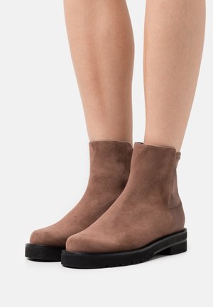 Bottines en daim marron avec un bout rond, des panneaux latéraux élastiques et une semelle en caoutchouc noire épaisse. Texture lisse et design minimaliste.