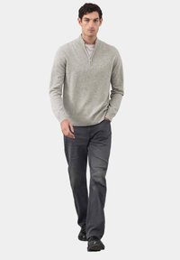 Grijze gebreide trui met een half-rits kraag, gecombineerd met donkere spijkerbroek. De outfit heeft een casual pasvorm en een zachte textuur, geschikt voor het dragen in lagen.