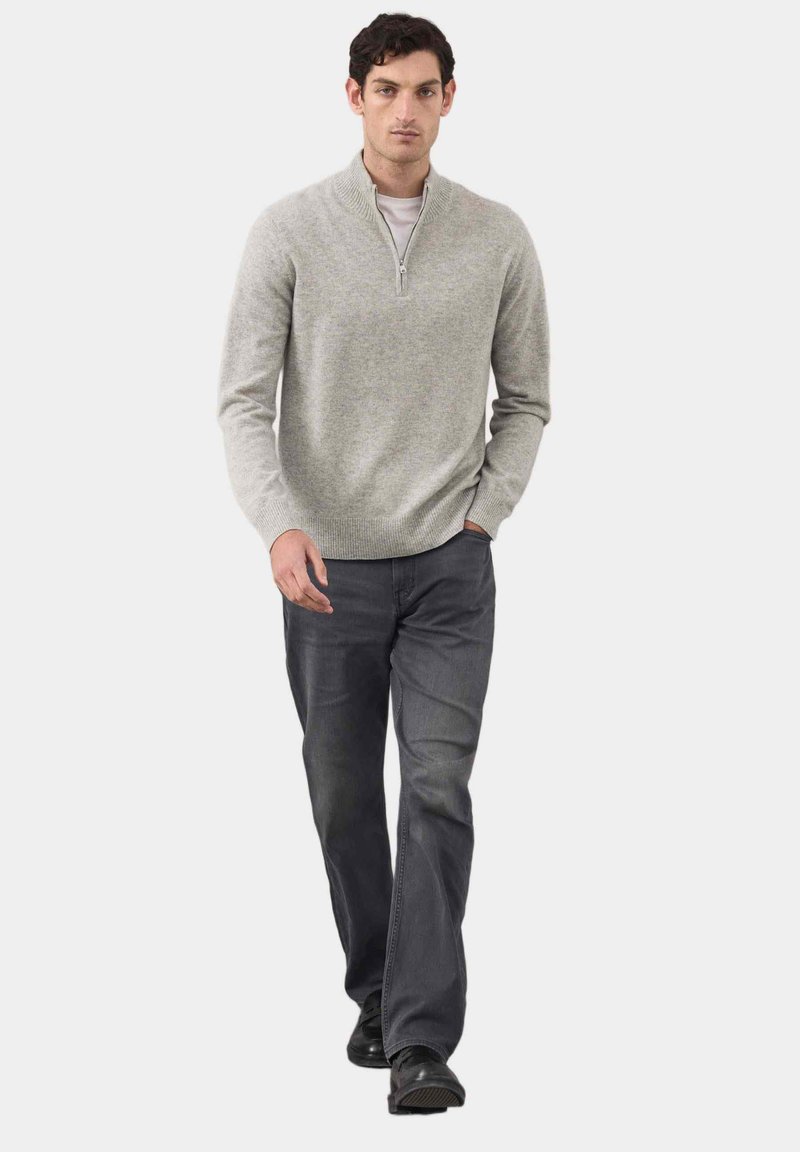 Grau gestrickter Pullover mit einem halben Reißverschluss am Kragen, kombiniert mit dunklen Jeans. Das Outfit hat eine lässige Passform und eine weiche Textur, die sich gut zum Schichten eignet.