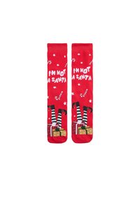 Calcetines rojos con el texto blanco "NO SOY UN SANTA", piernas de rayas negras y verdes, y gráficos de cajas de regalo. Hay estrellas y bastones de caramelo esparcidos.