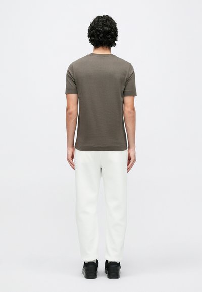 Olivovo zelené priliehavé tričko s krátkymi rukávmi; v kombinácii s bielymi teplákmi a čiernymi teniskami. Jednoduchý dizajn, plochá pletená textúra látky.