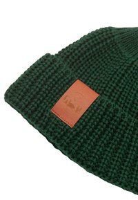 Zielona dzianinowa czapka z grubą teksturą, z brązową skórzaną łatką z logo. Projekt jest prosty i zaokrąglony u czubka.