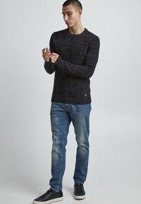 Sötét tengerészkék kötött pulóver hosszú ujjakkal, textúrált anyaggal és kerek nyakkivágással, világoskék farmernadrággal és fekete tornacipővel párosítva.
