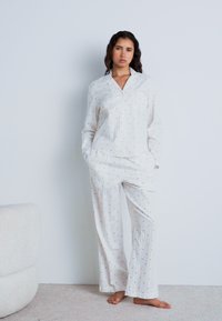 Set di pigiama bianco composto da una camicia con bottoni, colletto e maniche lunghe; decorato con piccoli puntini colorati e pantaloni larghi.
