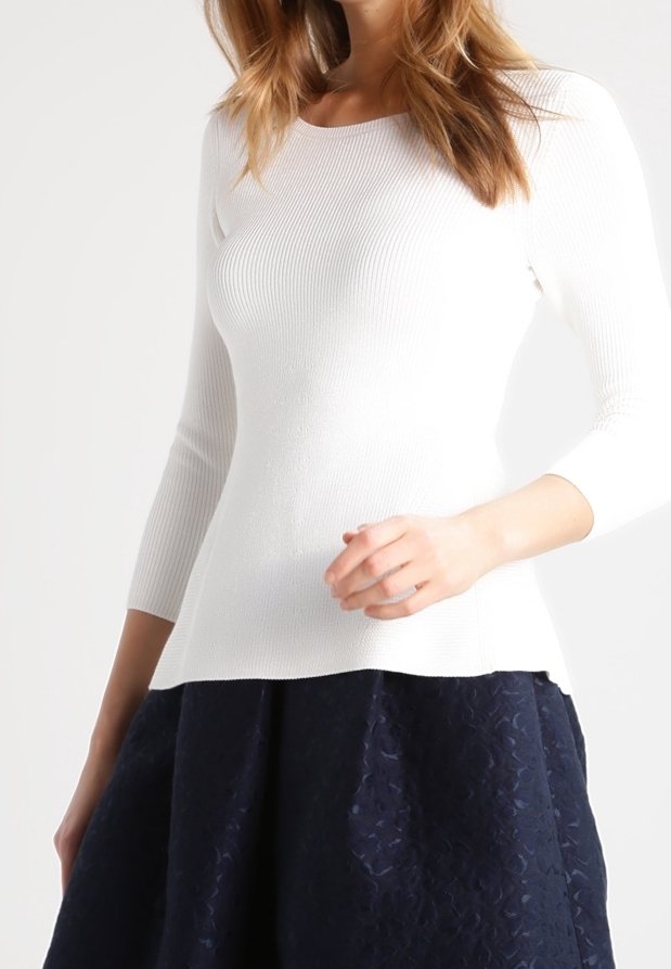 Weißes, geripptes Stricktop mit dreiviertel Ärmeln, verziert mit einem eng anliegenden Oberteil und einem ausgestellten Saum. Kombiniert mit einem dunklen, strukturierten Rock.