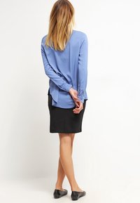 Blusa de manga larga azul claro con una textura suave, combinada con una falda negra. La blusa tiene un dobladillo curved y un ajuste relajado.