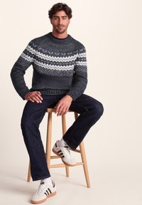 Knitted sweater with dark gray and white zigzag pattern, round neckline, and ribbed cuffs. Paired with dark jeans and casual sneakers.
