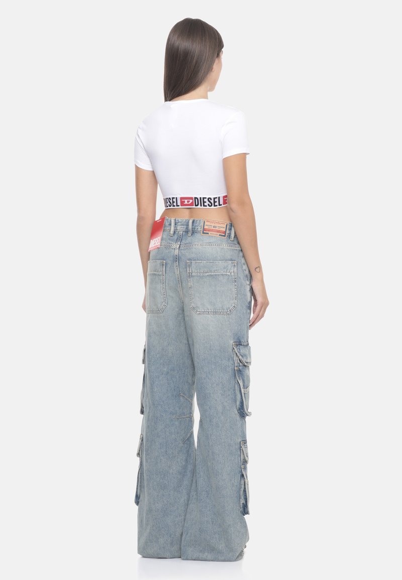 Pantaloni cargo in denim blu con una vestibilità ampia, dotati di grandi tasche laterali e di un alto punto vita. Abbinati a una t-shirt corta bianca.