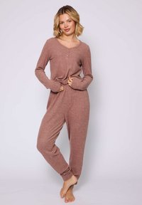 Rippstrick-Jumpsuit in Mauve mit langen Ärmeln, V-Ausschnitt und Knopfleiste. Mit enganliegenden Bündchen und entspannter Passform.