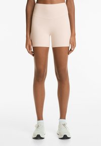 Ljusrosa elastiska träningsshorts med hög midja, slät textur och åtsittande design. Bärs med ljusa träningsskor.