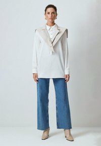 White long-sleeve shirt with a beige collar and buttons, paired with loose-fitting blue denim jeans and beige ankle boots.