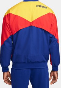 Chaqueta azul, roja y amarilla con un diseño de bloques de color. Presenta un cuello alto y puños elásticos, confeccionada en tejido suave. Incluye bordado en la parte posterior.