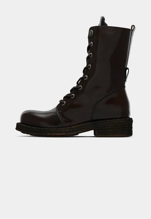 Braune Lederstiefelette mit glänzender Oberfläche, runder Zehenpartie, auffälliger Schnürung und einem robusten Holzstruktur-Absatz.